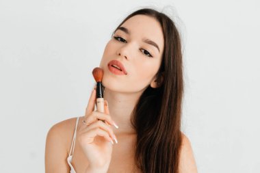 Kameraya bakan esmer model resmi ve beyaz arkaplanda izole edilmiş makyaj fırçası.