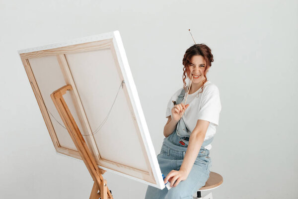 Female artist painting picture in her studio. Woman paints picture on canvas with oil paints in her studio