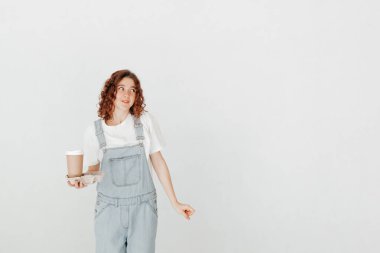 Tulumlu genç bir kadın, elinde bir fincan sıcak kahve, beyaz duvarın üstünde. Boş zaman kavramı