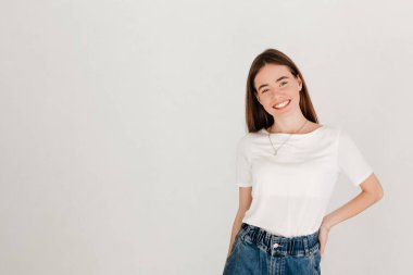 Beyaz tişört ve kot pantolon giyen, beyaz stüdyo duvarında izole edilmiş güzel bir kadının stüdyo portresi.