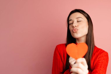 Güzel kız kırmızı kazak, siyah saç ve siyah manikür giyiyor. Kız pembe arka planda yalnız poz veriyor.