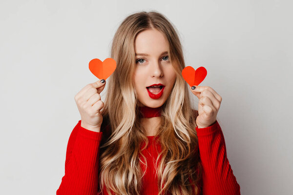 Woman holding paper hearts, posing over white studio background, smiling to the camera. Happy Valentine's holiday celebration