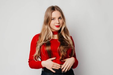 Genç ve güzel bir kadın randevuya hazırlanıyor, kırmızı kazak giyiyor, beyaz arka planda poz veriyor.