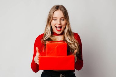 Mutlu genç kadın kırmızı kutularda iki hediye aldı, gülümsüyor, beyaz arka planda kırmızı üstte duruyordu.