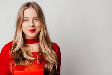 Mutlu genç bir kadın kırmızı kutuda bir hediye aldı, gülümsüyordu, beyaz arka planda kırmızı üstte duruyordu.