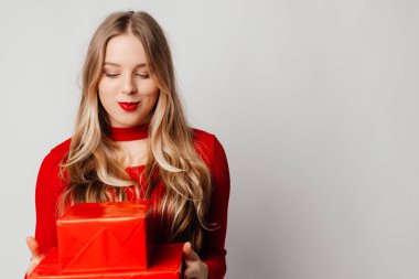 Mutlu genç kadın kırmızı kutularda iki hediye aldı, gülümsüyor, beyaz arka planda kırmızı üstte duruyordu.