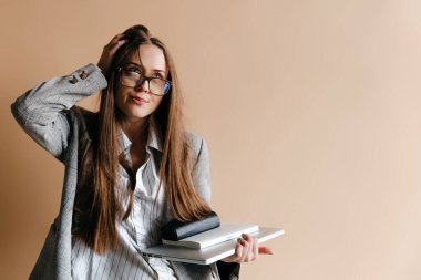 Büyüleyici iş kadını dizüstü bilgisayarını ve defterini tutuyor, gözlüklerine dokunuyor ve yukarı bakıyor.