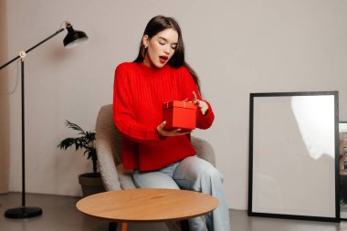 Kız ışık stüdyosundaki rahat sandalyede oturuyor. Kız kırmızı ruj ve kırmızı kazak giyiyor.