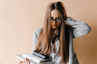 Çekici iş kadını dizüstü bilgisayar ve not defteri tutuyor, kafasına dokunuyor ve kameraya bakıyor.