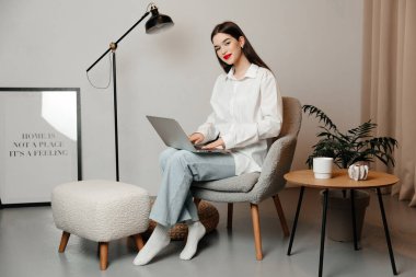 Kız kameraya bakıyor ve gülümsüyor. Genç bayan rahat bir elbise giyiyor.