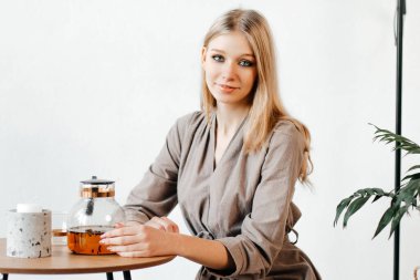 Şirin kız bir çaydanlık çay sipariş etti. Genç bayan küçük tahta bir masada oturuyor.