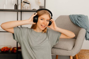 Çekici bir gülümsemesi olan kız ışık odasının zemininde oturuyor. Odada bir sandalye ve raf var.