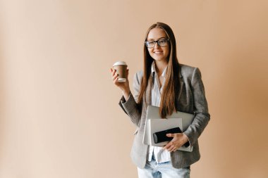 Gözlüklü gülümseyen iş kadını dizüstü bilgisayarını tutuyor ve kahve fincanını götürüyor. Serbest konsept