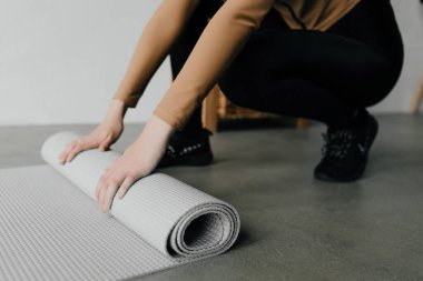 Yoga dersinden sonra genç bir kadının elleri gri paspası yuvarlıyor.