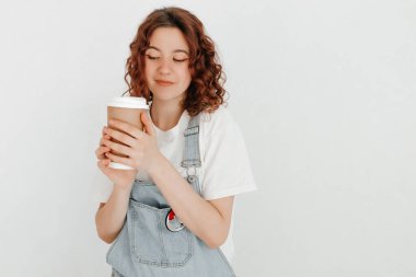 Tulumlu genç bir kadın, elinde bir fincan sıcak kahve, beyaz duvarın üstünde. Boş zaman kavramı