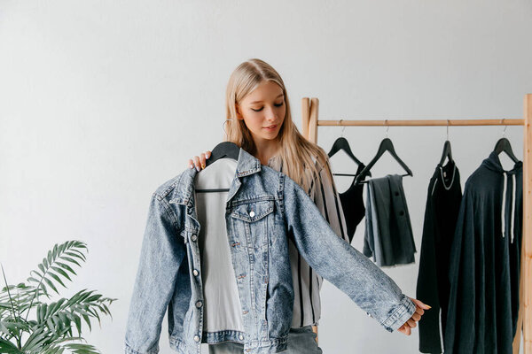 Young fashion vlogger trying on blue denim jacket, showing it on a hanger