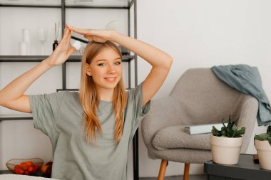 Güzel kız yerde oturuyor ve yeni dairesinde eşyaları yerleştiriyor. Kızın sarı saçları var ve gri bir tişört giyiyor.