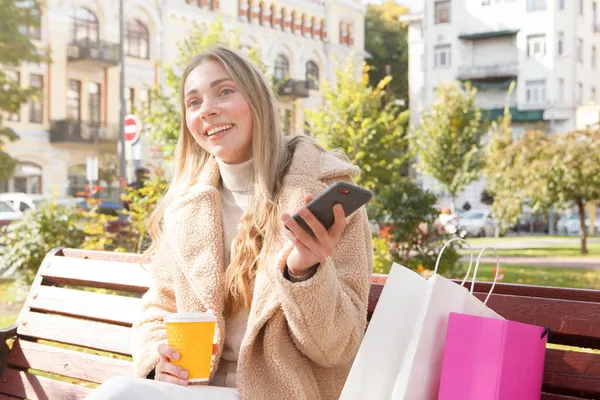 幸せな女性は 彼女のスマートフォンを使用して 暖かい秋の日に都市公園で休息を楽しんで笑って — ストック写真