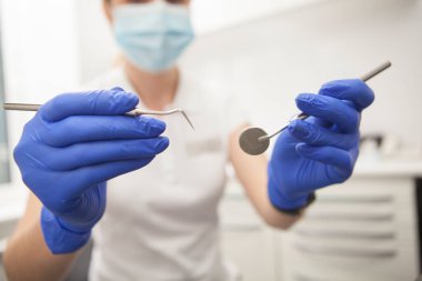 Kadın dişçinin kameraya dişçi aletleri tutarken çekilmiş.