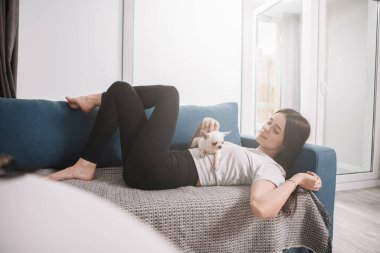 Genç ve rahat bir kadın evdeki köpeğiyle kanepede uzanıyor.