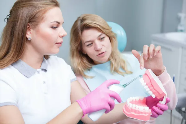 Młoda Dentystka Pokazuje Pacjentowi Ultradźwiękową Szczoteczkę Zębów Modelu Szczęki — Zdjęcie stockowe