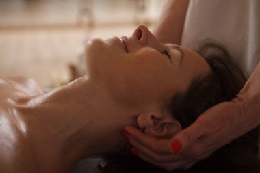 Gözleri kapalı gülümseyen orta yaşlı bir kadının kaplıcada profesyonel kafa masajı yaptırması.