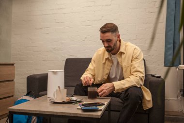 Yakışıklı sakallı adam kanepede dinleniyor. Evde ya da otelde kahve içiyor.