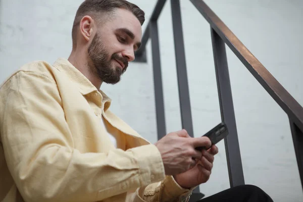 Yakışıklı Sakallı Adam Gülümsüyor Akıllı Telefon Uygulaması Kullanıyor Merdivenlerde Oturuyor — Stok fotoğraf