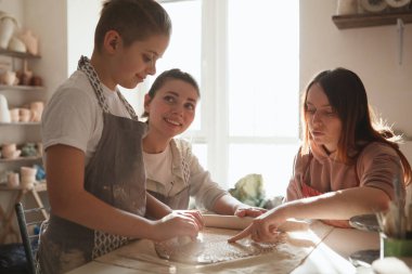 Genç bir çocuk, annesi ve profesyonel çömlekçi ile çömlekçilik dersinde seramik yapıyor.