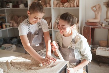 Güzel bir kadın gülümsüyor, oğlunu çömlekçilik dersinde kil ile çalışırken izliyor.