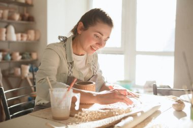 Güzel kadın gülümsüyor, çömlek atölyesinde sabah gün ışığında kille çalışıyor.