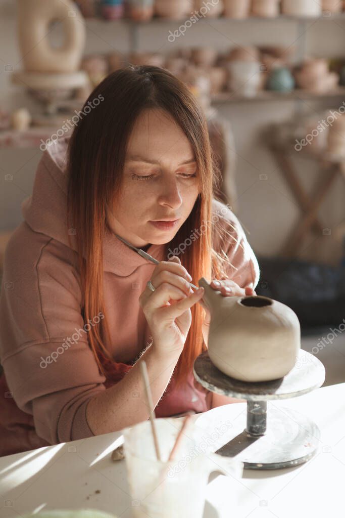 Vertical shot of a female potter working at her art studio, making a teapot