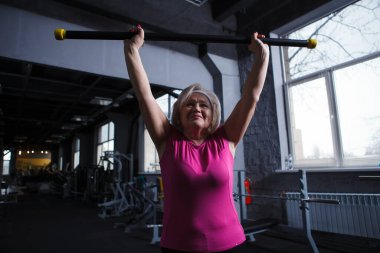 Güçlü, sağlıklı, yaşlı kadın halter kaldırıyor, göğüs masajı yapıyor.