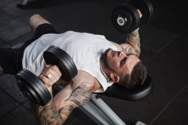 Top view shot of a strong muscular sportsman exercising with dumbbells at gym
