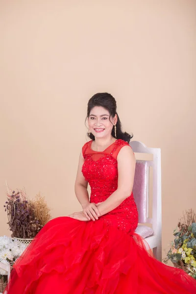 Piękna Azjatka Dorosła Kobieta Czerwonej Sukience Siedzi Fotelu Studio Kwiatami — Zdjęcie stockowe