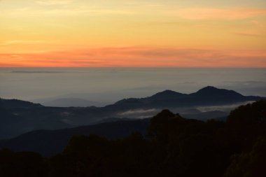 Güneş sık bir ormanın arkasında batıyor ve ardından dağlar geliyor.