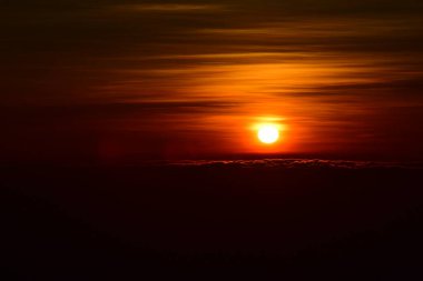 Güneş sık bir ormanın arkasında batıyor ve ardından dağlar geliyor.