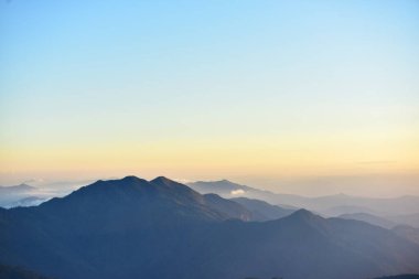 Yoğun bir orman bölgesinin ardında batan bir güneşin resmi. Ardından dağlar..