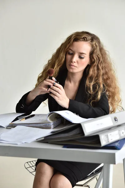 Woman in formal wear doing makeup at workplace.