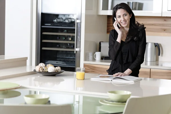 Женщина на мобильном телефоне на кухне — стоковое фото