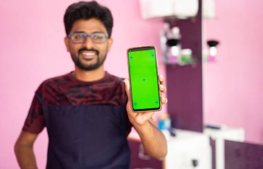 Babrer 'dan Smatphone' a, iş kıyafetleri satan genç berber Showig cep telefonlu yeşil ekranlı salon - reklam konsepti, küçük işletmeler, teknoloji ve internet