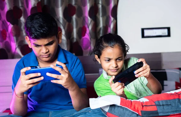 Siblings busy playing video game on mobile phone during night sleep - concept of kids gaming addiction, childhood lifestyles and technology. — стоковое фото