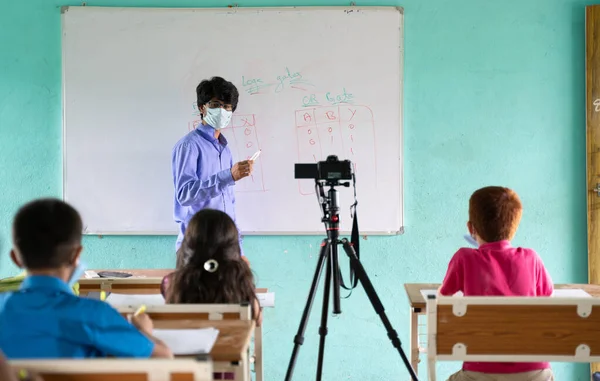 Teacher in medical mask with limited kids teaching and streaming live classes to students at classroom during coronavirus covid-19 pendamic - Concept of new normal, Education and back to school. — Stock Fotó