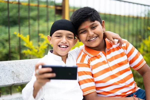 Dos niños multiétnicos felices tomando selfie en el teléfono móvil en el parque - concpet de amistad, diversidad religiosa y armonía social — Foto de Stock