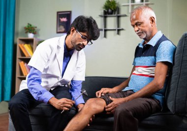 Ortopedi doktoru ya da doktor yaşlı bir adamın diz eklem ağrısını evde diz çekiçle kontrol ediyor - eklem iltihabı, sağlık ve yaralanma tedavisi kavramı.