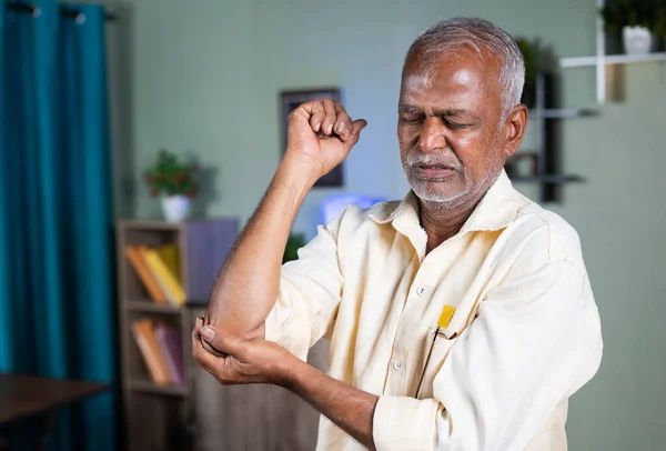 Anciano anciano indio que se ejercita apretando la mano debido al dolor en las articulaciones del codo en el hogar - concepto de dolor en las articulaciones y lesión por esguince. — Foto de Stock