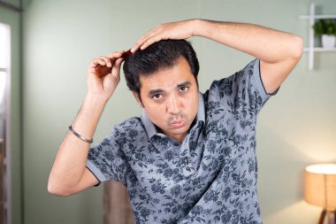 Genç ve yakışıklı bir adam şarkı söyleyerek eğlenirken kameraya evde bakmak - saç stili tımarlama ve kendine bakım kavramı.