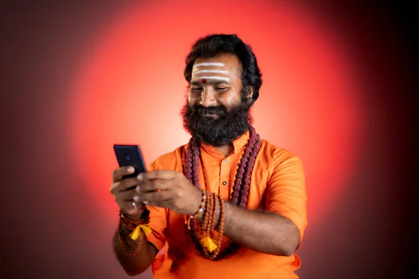 Holy Indian god man busy using social media on mobile phone at monastery - concept of Mobile astrologer service , technology and internet. — Stockfoto