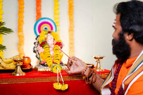 Céntrate en la mano Hombre dios santo o sacerdote indio que ofrece aarti cantando himnos frente al ídolo de lord ganesh durante la celebración del festival en casa - concepto de festival tredicional y cultura india. —  Fotos de Stock