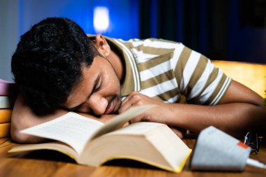 Evde okumak için okumaktan yorulduğu için masada uyuyan genç öğrenci - sıkı çalışma, tembellik ve gece geç saatlere kadar çalışma kavramı